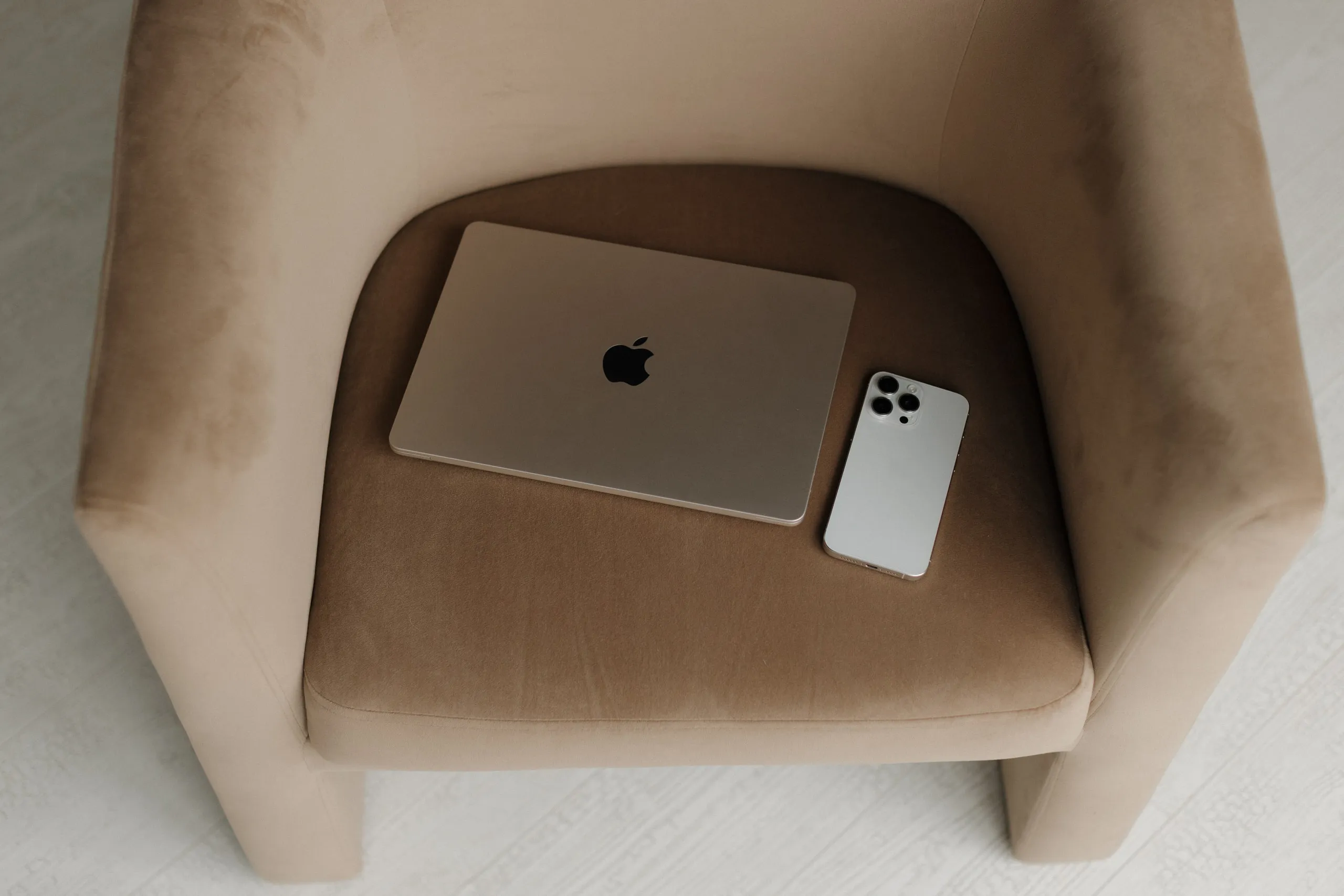 Laptop and phone resting on a taupe velvet chair